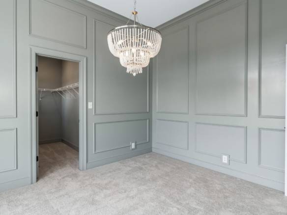 Interior of a modern gray-walled bedroom featuring a chandelier and walk-in closet.
