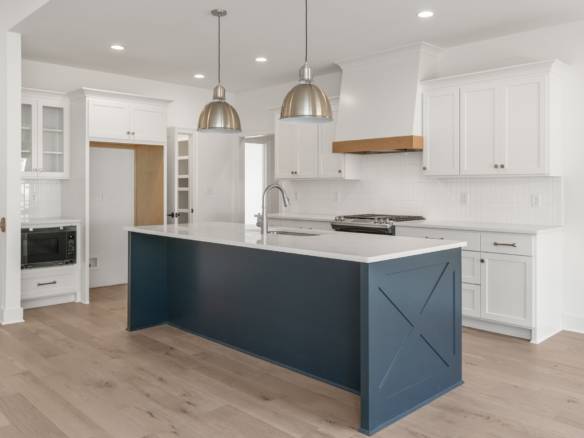 Modern white kitchen with navy island and pendant lighting.