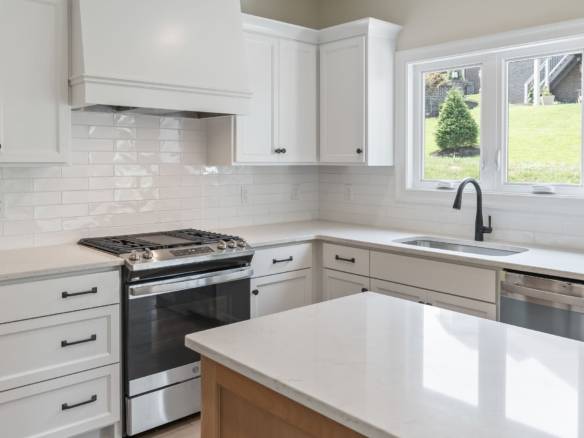 White kitchen with sleek cabinets and a spacious island, featuring a large window overlooking a gree.