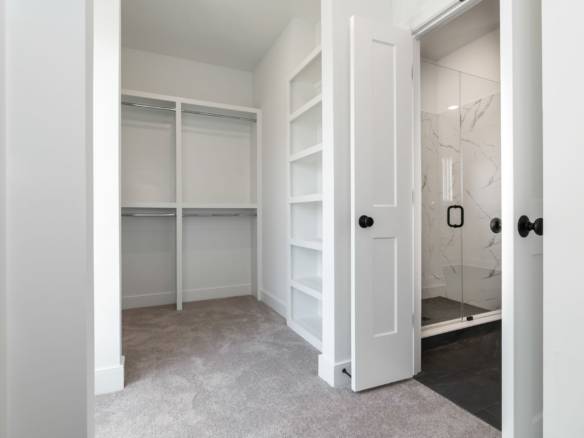 Walk-in closet with built-in shelves and a glass shower in a contemporary master bedroom.