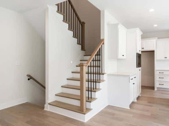 Staircase with wooden steps and black metal balusters in a bright, open kitchen area.