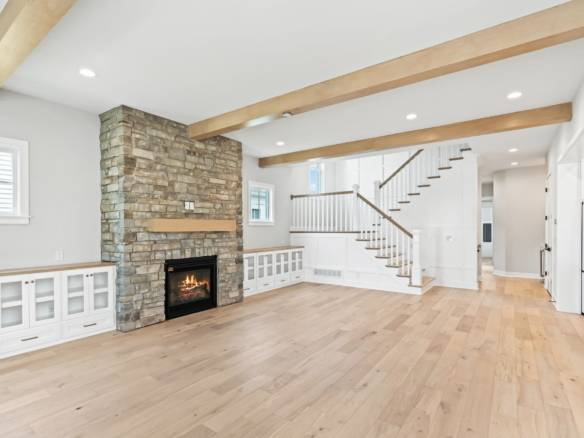 Spacious living area featuring a stone fireplace, wooden beams, and bright natural light.