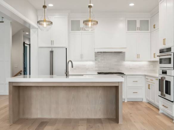 Modern white kitchen with island and gold accents, featuring sleek cabinetry and stainless steel app.