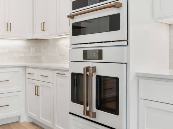 Built-in white kitchen oven and microwave with gold handles.