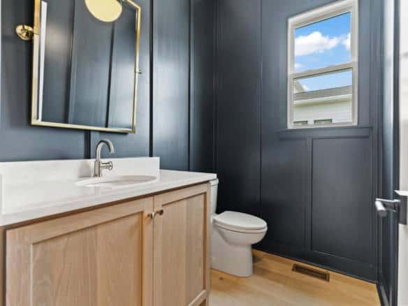 Bright bathroom featuring navy blue walls, a white vanity, and a window with a view.