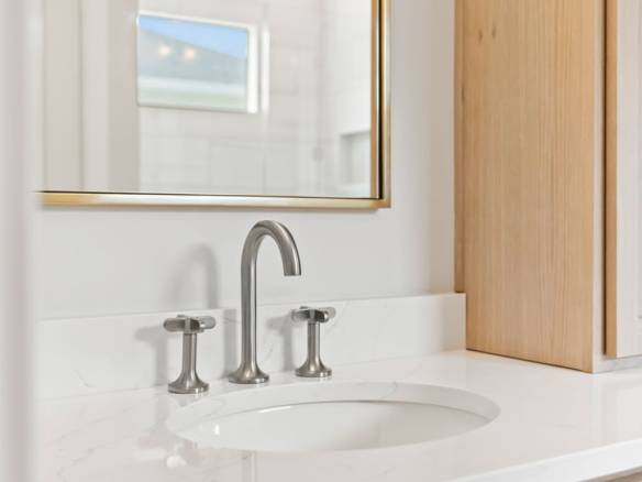 Bathroom vanity with white countertop, mirror, and wooden cabinets.
