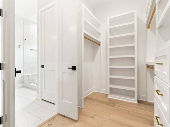 Walk-in closet with white built-in shelves and drawers, adjacent to a bathroom at 6331 Pond Lily Str.