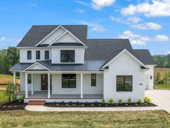 New construction home with white exterior, black roof, and front porch.