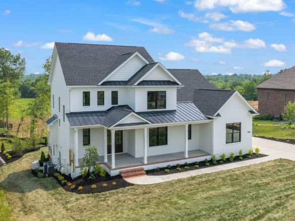 New white farmhouse with front porch and black metal roof, under a blue sky.