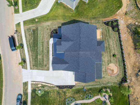 Aerial view of a newly constructed house with a dark roof, driveway, and landscaped yard at 17423 Sh.