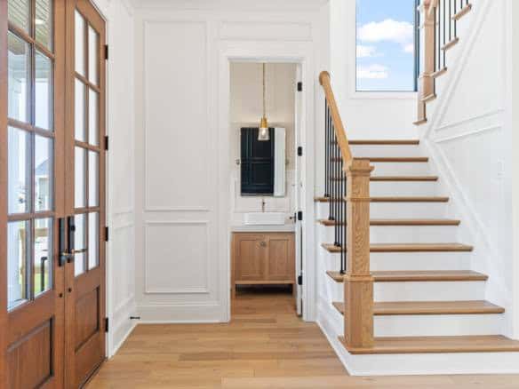Bright interior with white walls, wooden stairs, and a glass-paneled entry door.