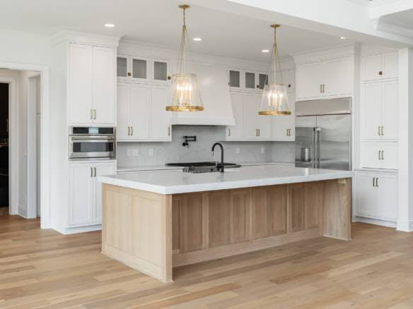 Modern white kitchen with island, pendant lights, and stainless steel appliances.