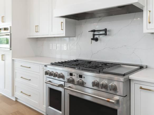 Modern white kitchen with marble backsplash and stainless steel stove.