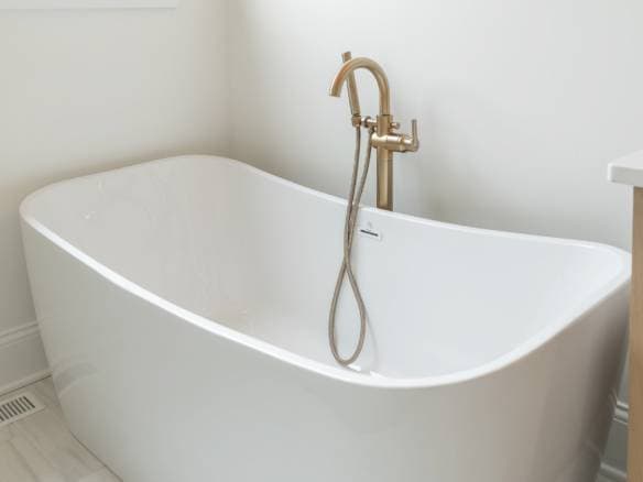 Freestanding white bathtub with gold fixtures in a bright bathroom.