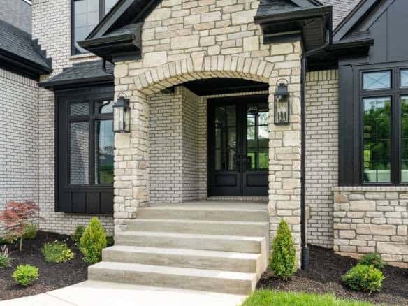 Elegant brick house entrance with steps and black accents, landscaping included.