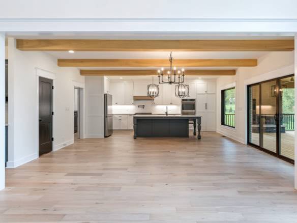 Spacious kitchen featuring wooden beams, white cabinetry, stainless steel appliances, and large slid.