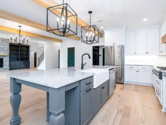 Modern kitchen with white cabinets and a large island, featuring stylish lighting and stainless stee.
