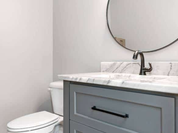Bathroom with marble countertop, blue vanity, and round mirror.
