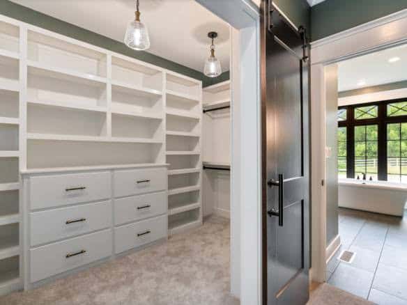 Walk-in closet with white shelving and drawers, adjacent to a bright bathroom with a bathtub at 1110.