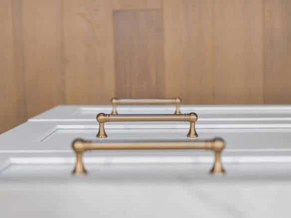 White kitchen cabinet with gold handles and wooden wall background.