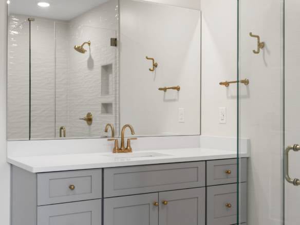 Modern bathroom vanity with gold fixtures and a glass shower enclosure.