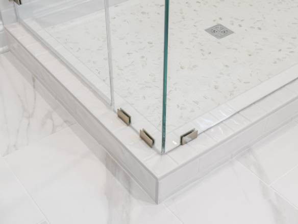 Shower glass enclosure with metal clamps and tiled base.