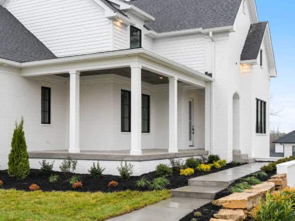 Modern white house with a spacious front porch and landscaped yard.