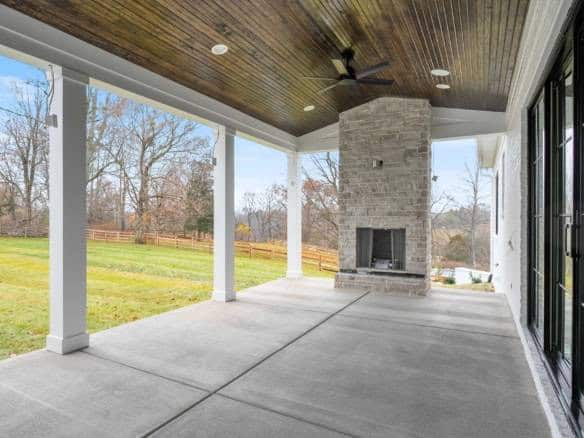 Spacious covered patio with fireplace and scenic backyard view.