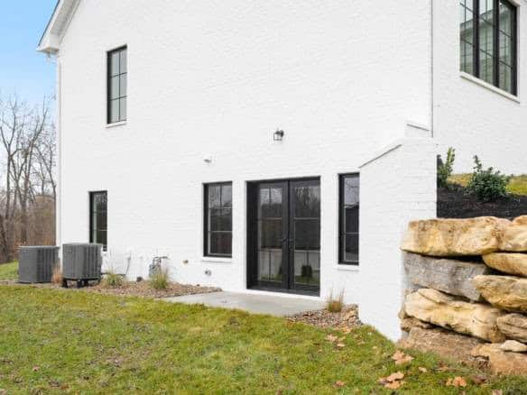 Modern white house exterior with black-framed windows and a stone retaining wall.