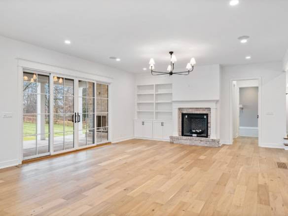 Spacious living room featuring a fireplace, built-in shelves, and large sliding glass doors opening.