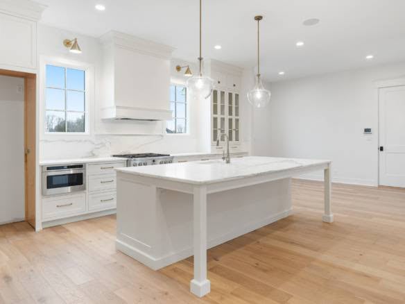 Modern white kitchen with island, pendant lights, and large windows for bright, open space.