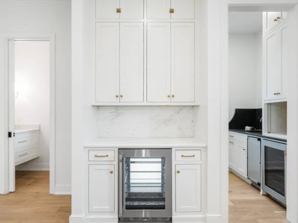 White kitchen cabinets with marble backsplash and wine cooler, bright and elegant design.
