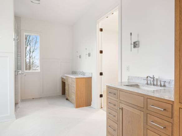 Bright bathroom featuring white walls, natural light, and wooden vanity cabinets.