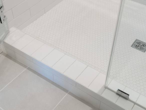 Bathroom shower with white tile and glass door, featuring a sleek drain and clean design.