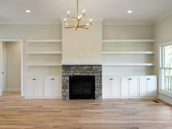 Beautiful living room featuring a stone fireplace, white built-in shelves, and large windows for nat.