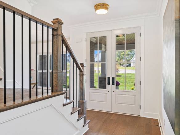 Entryway with white door and glass panels, wooden flooring, and staircase railing.