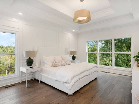 Spacious bedroom featuring white walls, a cozy bed, and large windows offering natural light and sce.