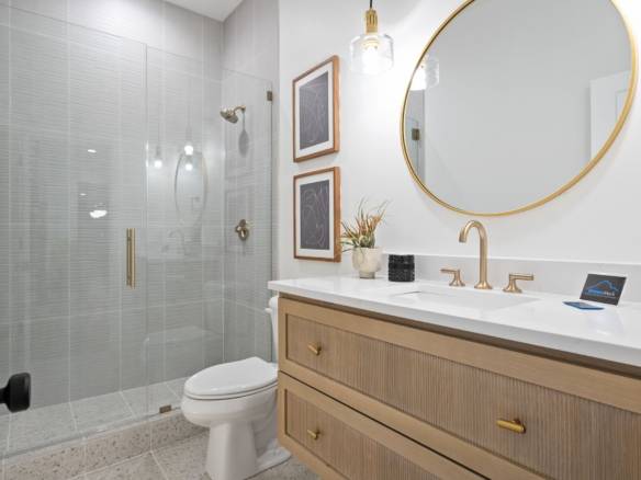 Bathroom with glass shower, wooden vanity, and gold fixtures.