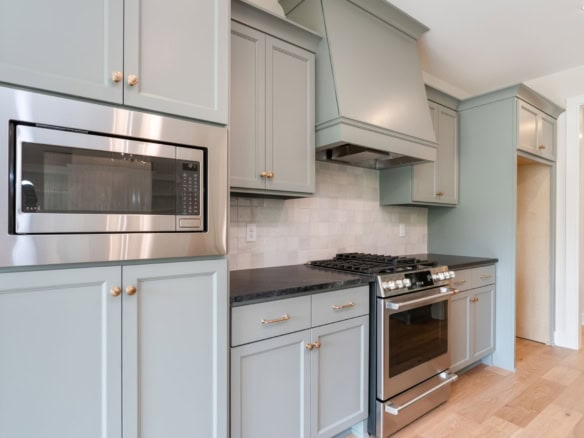 Bright kitchen featuring light blue cabinetry, stainless steel microwave, and oven.