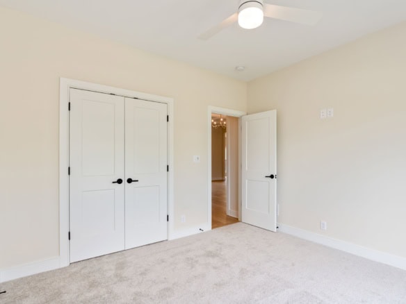 Bright, empty bedroom with white walls, double closet doors, and beige carpet flooring.