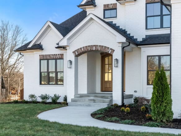 Modern white brick house with a welcoming front porch and landscaped yard.