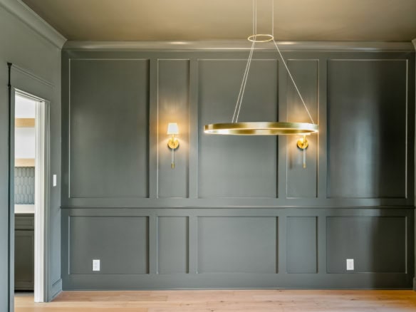 Interior wall with gray paneling, wall sconces, and a contemporary chandelier.