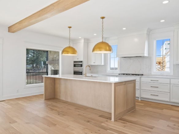 Bright, spacious kitchen featuring white cabinetry, a large island, and elegant gold pendant lightin.
