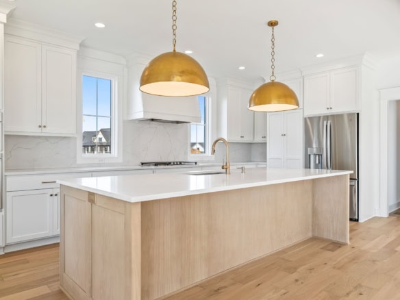 Modern white kitchen with a large island, gold pendant lights, and ample natural light.