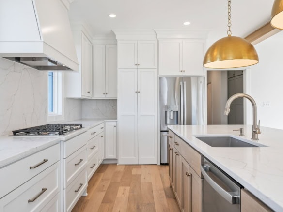 Bright, contemporary kitchen featuring white cabinetry and gold pendant lighting.