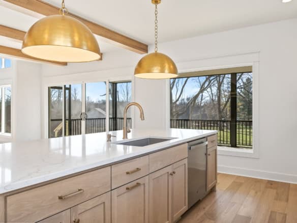 Bright, spacious kitchen featuring large windows, white cabinetry, and elegant gold pendant lighting.