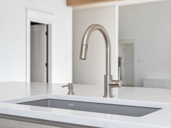 Modern kitchen sink with stainless steel faucet and white marble countertop.