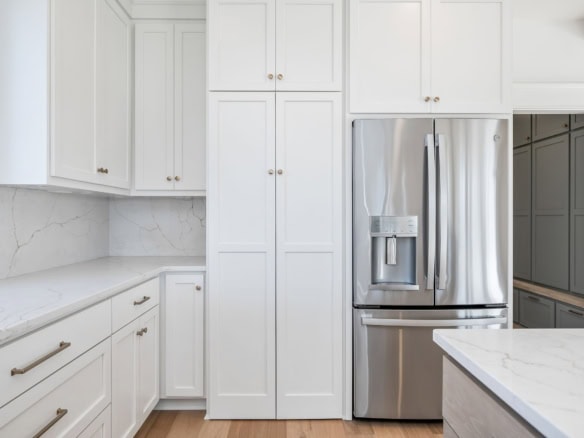 Modern white kitchen with stainless steel refrigerator and marble countertops.
