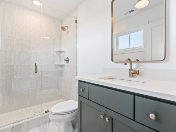 Elegant bathroom featuring white tiled shower and navy vanity with gold fixtures.