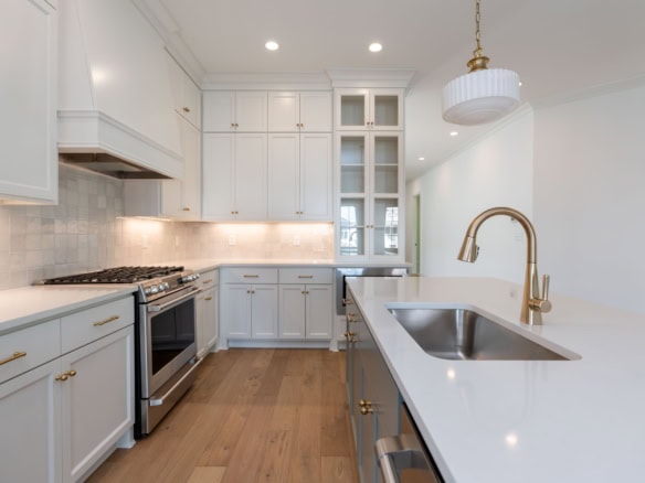 Modern kitchen with white cabinets, gold hardware, and stainless steel appliances.